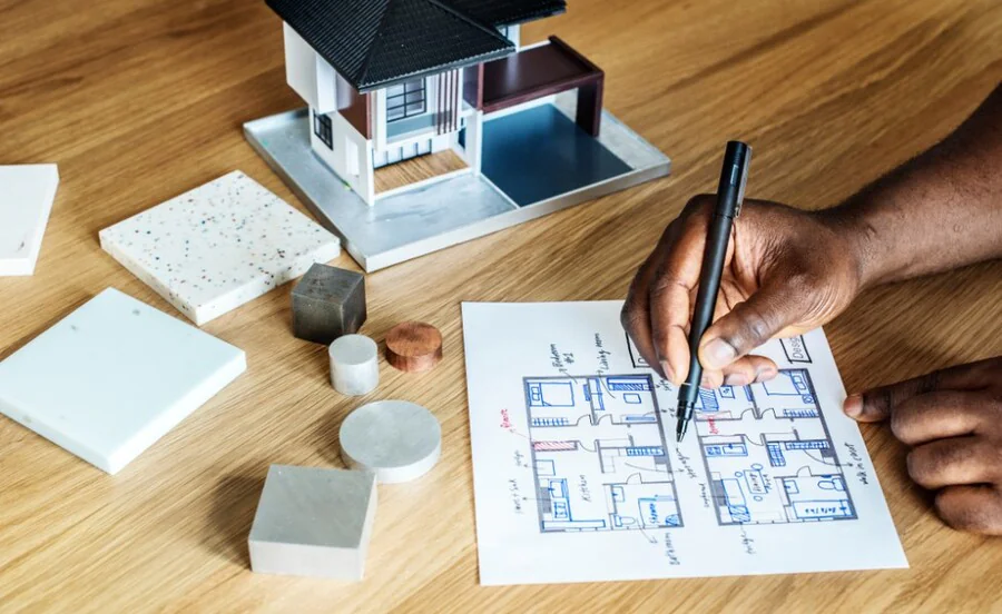 Plan d'un logement dessiné à la main à côté d'une maquette de maison et d'échantillons de matériaux, pour préparer un projet de rénovation
